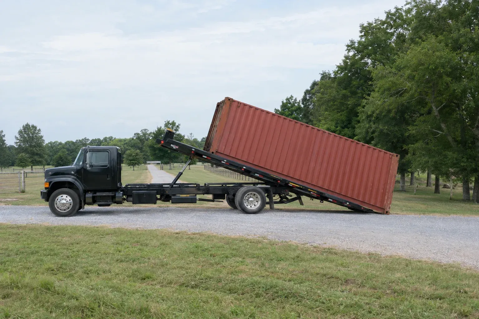 A tilt-bed truck sliding a container onto a gravel driveway
