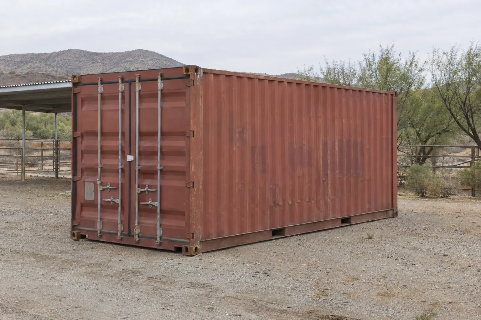 Used red 20ft container beside a horse corral on desert acreage outside New Mexico