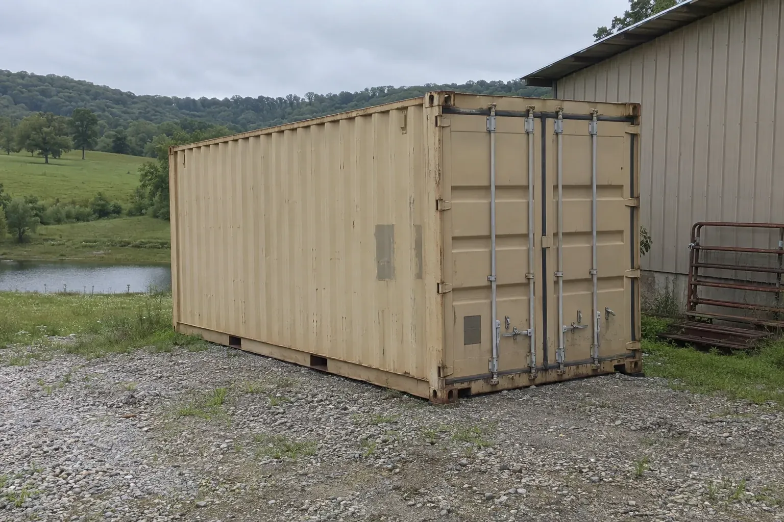 Used tan 20ft container by a metal barn in rolling wooded hills outside Kentucky