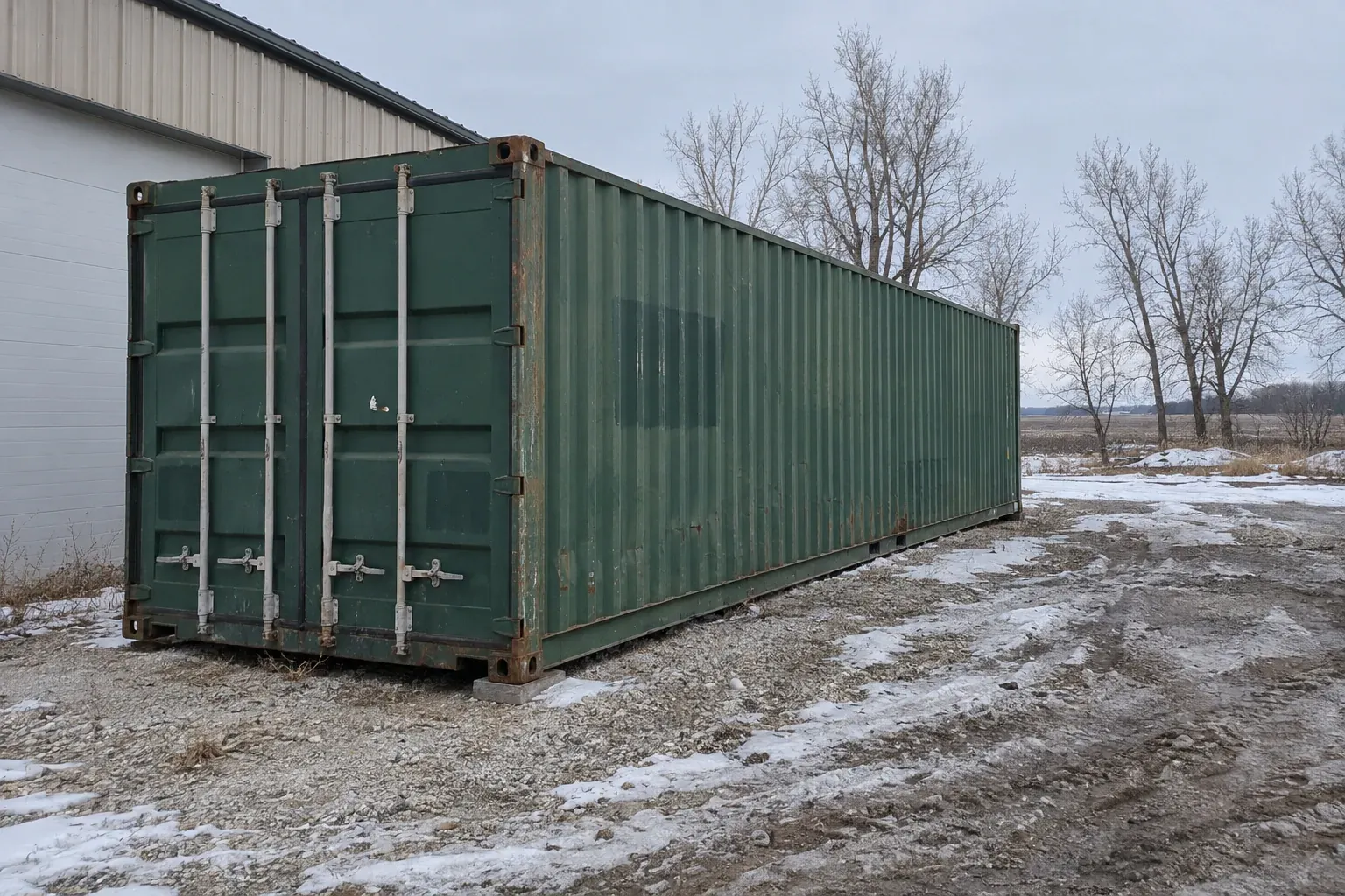Used green 40ft container beside a pole barn with old snow on the ground outside Illinois